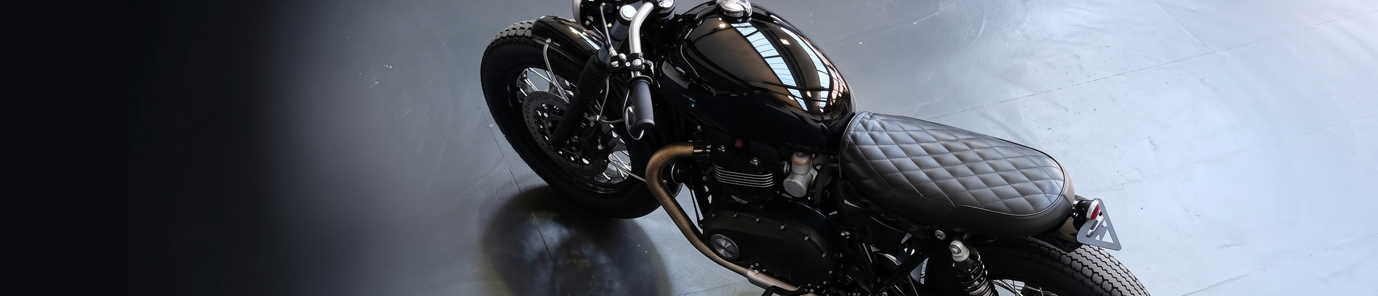 Moto vue de profil dans un atelier, avec selle, sacoche et soufflets de fourche en cuir.